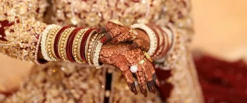 Heavy full-hand bridal mehndi design with deep maroon stain and floral jaali patterns, paired with red and gold bridal bangles
